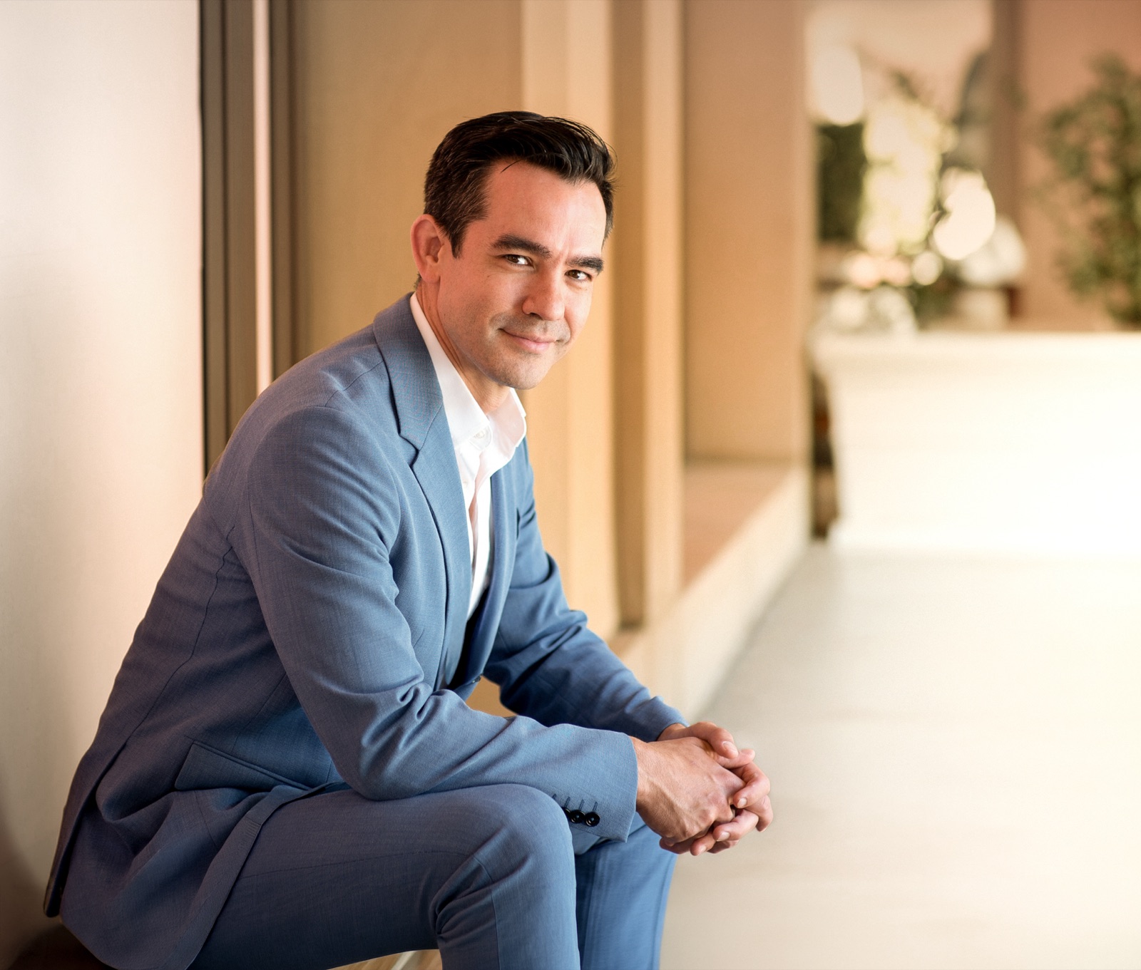 Dr. Nicholas Lahar seated in a sunlit corridor, wearing a blue suit